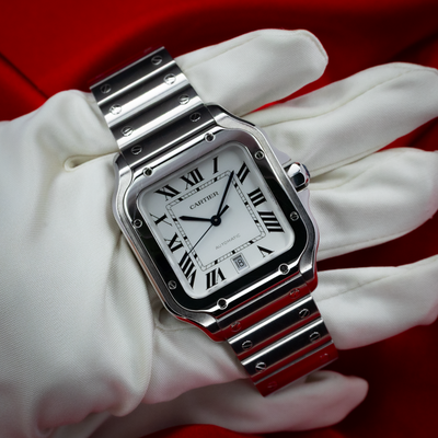 Cartier Santos De Cartier WSSA0018 on white-gloved hand showing the white dial with Roman numerals and metal bracelet.