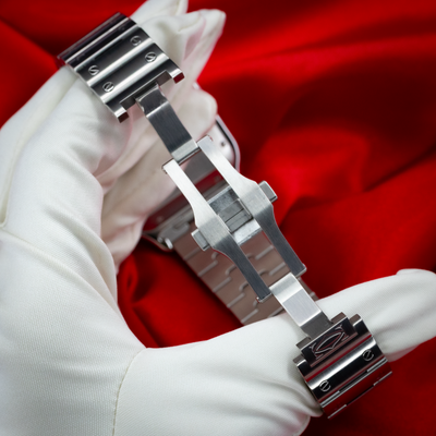 Cartier Santos De Cartier WSSA0018, stainless steel folding clasp and bracelet held by a gloved hand.