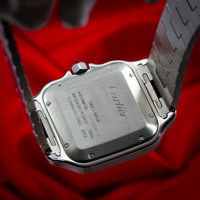 Cartier Santos De Cartier WSSA0018 caseback with engraved text and crown, bracelet attachment visible against red.