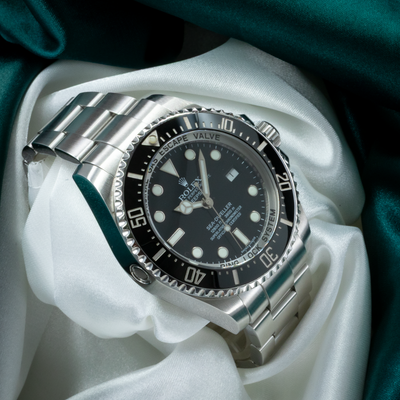 Rolex Sea-Dweller Deepsea 126660 dial, hands, date window, bezel, and steel bracelet on white and green silk.