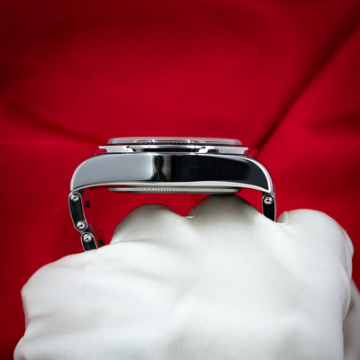 Tudor Black Bay Chrono M79360N-0002 watch case side profile on a white gloved hand, red background.