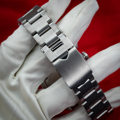 Tudor Black Bay Chrono M79360N-0002 clasp on a brushed metal bracelet on a white-gloved hand.
