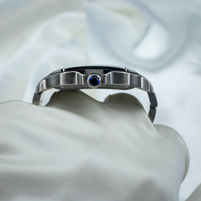 Cartier Santos WSSA0063 side profile, crown with blue cabochon, brushed steel case and bracelet on a white glove.