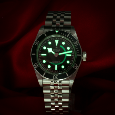 Tudor Black Bay 41mm M7941A1A0NU-0003, full watch view glowing in the dark, highlighting the dial and hands.