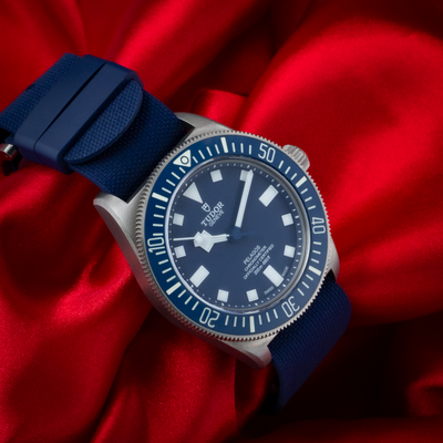 Tudor Pelagos FXD Marine Nationale 25707B/23-0001 with blue dial and bezel on red fabric with blue strap.