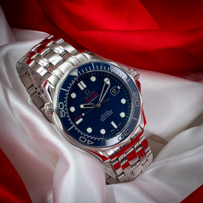 Omega Seamaster Diver 212.30.41.20.03.001 blue dial with date window, crown, and bracelet on red and white fabric.