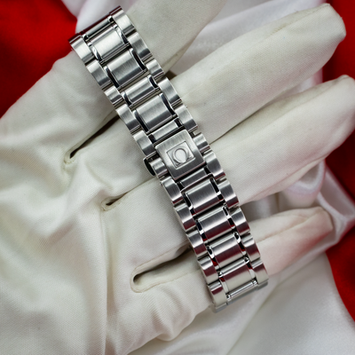 Omega Speedmaster Date 3513.30.00 clasp and stainless steel bracelet with an engraved Omega logo, worn on a white glove.