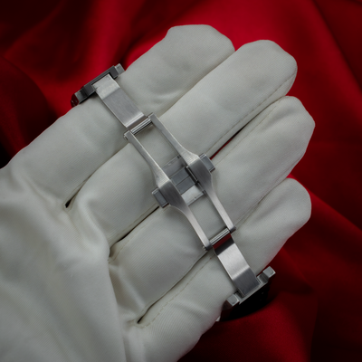 Cartier Santos De Cartier WSSA0029, brushed steel deployant clasp on a white-gloved hand against red fabric.