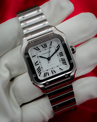 Cartier Santos De Cartier WSSA0029 watch with white dial, black Roman numerals, and brushed steel bracelet on a gloved hand.