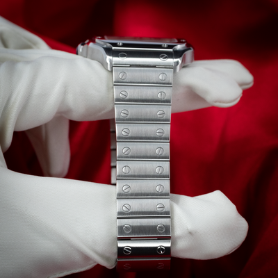 Cartier Santos De Cartier White Dial WSSA0029 bracelet, with screws visible, held by a white-gloved hand against a red