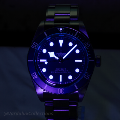 Tudor Black Bay 58 79030B dial with prominent blue lume on indices and hands in low light.