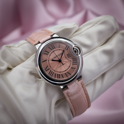 Cartier ballon bleu wsbb0002, closeup of the pink guilloché dial with black Roman numerals and hands, set on a white-gloved