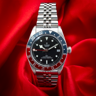 Tudor Black Bay GMT 79830RB, front view of the watch dial, bezel, and jubilee bracelet on red fabric.