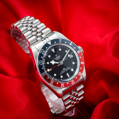 Tudor Black Bay GMT 79830RB, angled full dial view with the jubilee bracelet visible on a red background.