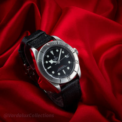 Tudor Black Bay 79730-0005, watch and strap on red fabric, showing the black dial, bezel, and textured black leather strap.