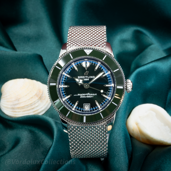 Breitling SuperOcean Heritage B31 AB31100361L1A1 watch with green dial and silver mesh bracelet on teal fabric.