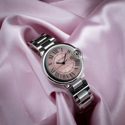 Cartier Ballon Bleu W6920100 watch with pink dial and metal bracelet on pink fabric.