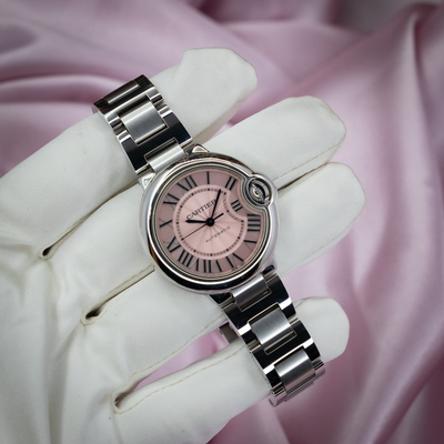 Cartier Ballon Bleu W6920100 watch, front view of pink dial and metal bracelet held by gloved hand.