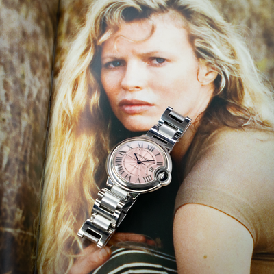 Cartier Ballon Bleu W6920100 watch on an open magazine, showing the pink dial, silver case, and metal bracelet.
