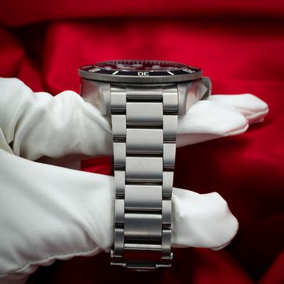 Tudor Pelagos 25500TN, side view of case, bezel, and bracelet with white gloved hand on red background.