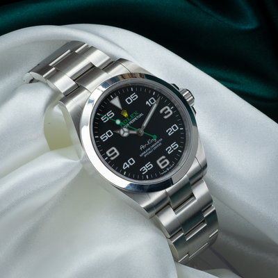 Rolex Air King Automatic Black Dial 126900, angled dial and bracelet on white and dark green fabric.