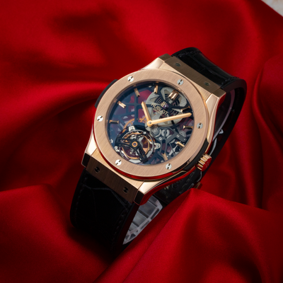 Hublot Gold Skeleton 505.OX.0180.LR, dial and gold case visible on a red background.